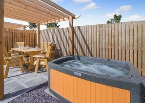 Una terraza de madera con un jacuzzi, una mesa y sillas.