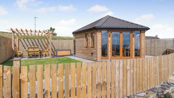 A wooden cabin with a fenced backyard, a pergola, and a hot tub.
