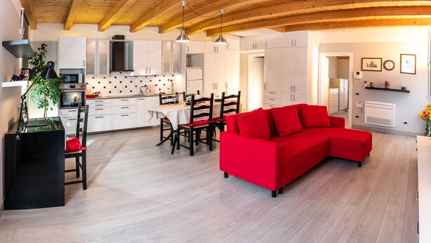 A modern kitchen with white cabinets, a dining area with a red sofa, and wooden flooring. - Charming apartment with private parking near the Cremona Racing Circuit (Casteldidone)
