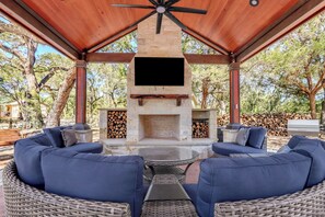 Un patio exterior con chimenea de piedra, asientos con cojines azules y un televisor de pantalla plana sobre el hogar.