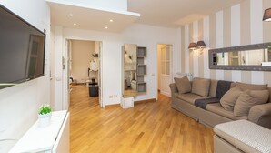 A modern living room with a wooden floor, a beige sofa, a white side table, and a large mirror on the wall. - Rental in Rome Vittoria Apartment (Rome)