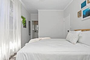 A bedroom with a large bed, a wooden headboard, a bedside table, and a mirror. - Reef Retreat Modern Beach HouseSanctuary (Port Noarlunga)