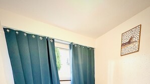 Un letto rifatto con lenzuola bianche in una stanza con una finestra coperta da tende azzurre.