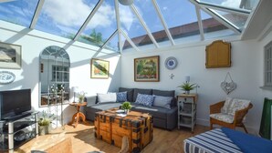 A sunlit room with a glass ceiling, a sofa, a wooden coffee table, a wicker chair, and a television. - 2 Bed in Stiffkey (oc-1892) (Stiffkey)