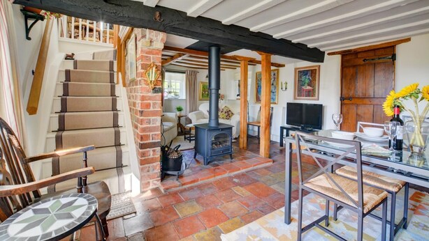 A cozy living room with a fireplace, a dining table, and a staircase. - 2 Bed in Stiffkey (oc-1892) (Stiffkey)