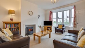 A cozy living room with a fireplace, leather sofas, a bookshelf, and a television. - 4 Bed in Leyburn (oc-ds370) (Leyburn)
