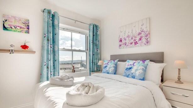A bedroom with a large bed, a window with curtains, a bedside table with a lamp, and artwork on the walls. - 4 Bed in Leyburn (oc-ds370) (Leyburn)