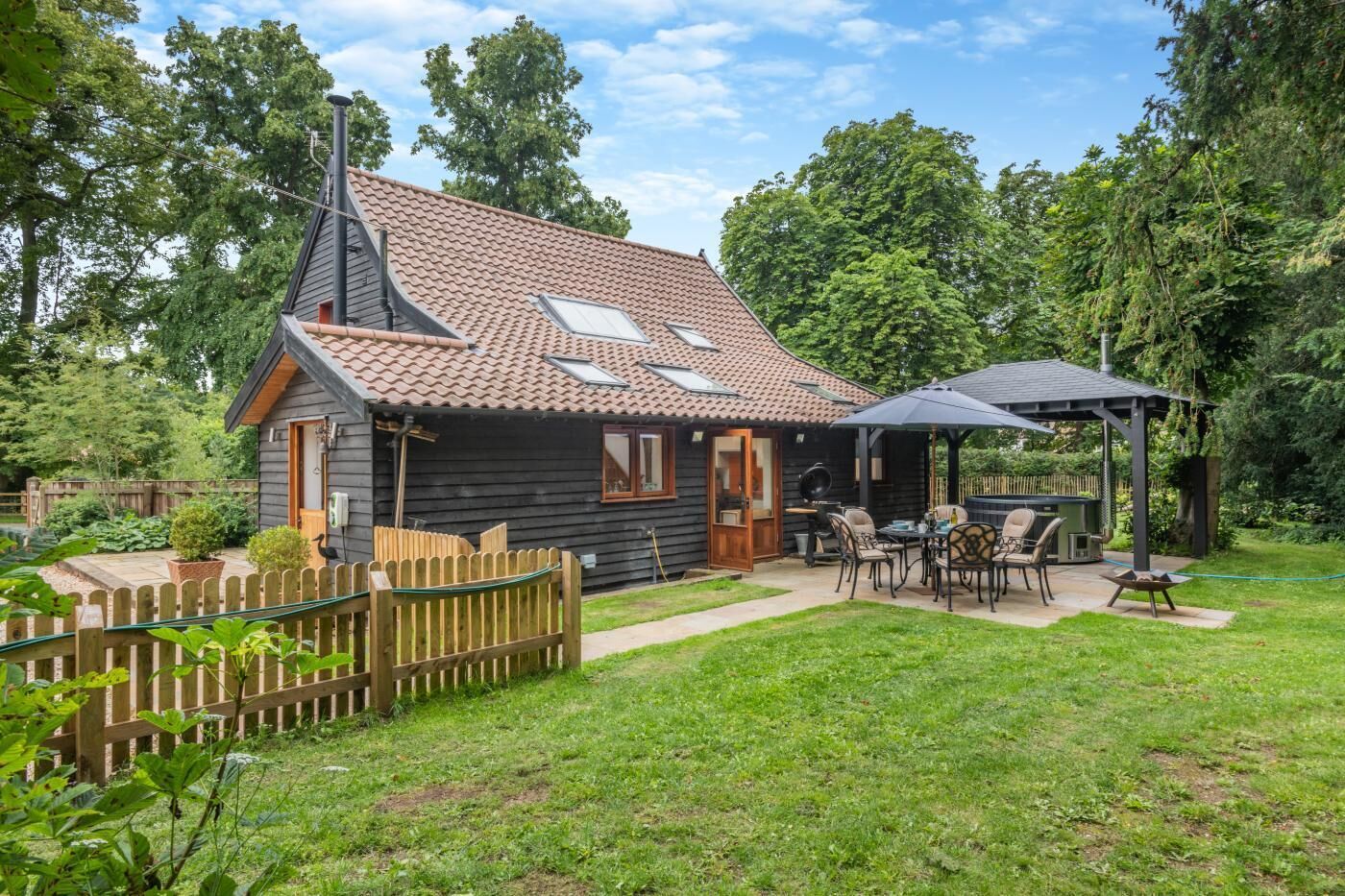 Een houten blokhut met pannendak, een houten terras en een patio met tuinmeubilair.
