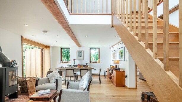 A spacious living area with a high ceiling, wooden staircase, and a cozy seating arrangement.