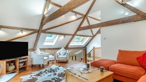A loft-style room with a sloped ceiling, wooden beams, a TV stand, seating area, and a cowhide rug.