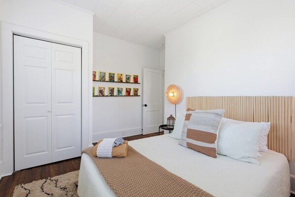 A bedroom with a bed, a bedside table, a lamp, and a wall with framed pictures.