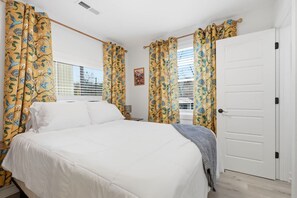 A bedroom with a bed, curtains, a door, and a window with blinds.