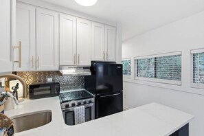 A modern kitchen with white cabinets, a black refrigerator, a microwave, and a stove.