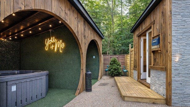 A wooden building with a neon sign reading 'You + Me,' a hot tub, and a wooden deck. - Cute Cabin, 2 Queens W Shared Hot Tub + Sauna (Easley)