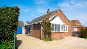 Une maison à deux étages, construite en briques, avec un garage à l’avant, une véranda et une allée gravillonnée.