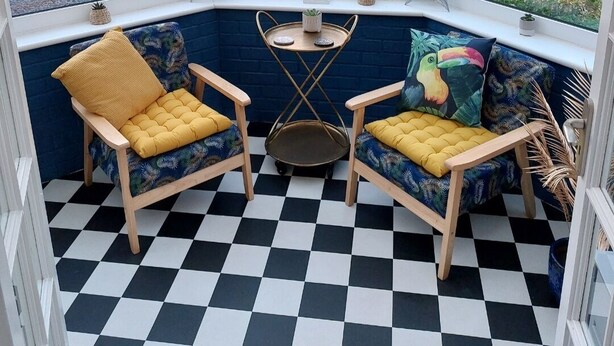 Une véranda avec un sol à carreaux, deux chaises en bois dotées de coussins jaunes, une petite table et une figurine d’hippocampe décorative.