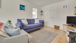 Un salon moderne avec un canapé bleu, un fauteuil gris, un téléviseur à écran plat posé sur un meuble en bois et une porte blanche.