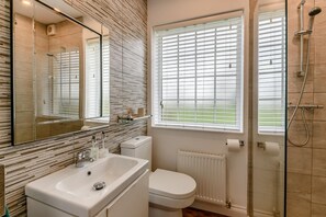 Ein modernes Badezimmer mit einer Duschkabine aus Glas, einer weißen Toilette und einem großen Spiegel über dem Waschbecken.