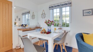 A modern kitchen with a dining area, featuring a white table, grey chairs, and a blue sofa with a yellow pillow. - 1 Bed in Hinderwell (oc-wa068) (Port Mulgrave)