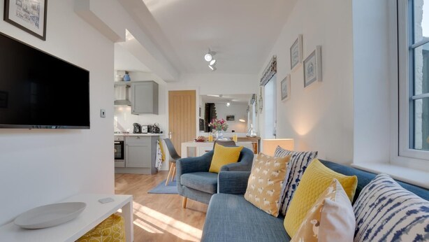 A modern living room with a grey sofa, yellow cushions, and a flat-screen TV. - 1 Bed in Hinderwell (oc-wa068) (Port Mulgrave)