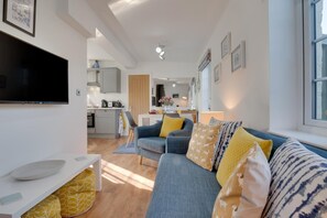 A modern living room with a grey sofa, yellow cushions, and a flat-screen TV. - 1 Bed in Hinderwell (oc-wa068) (Port Mulgrave)