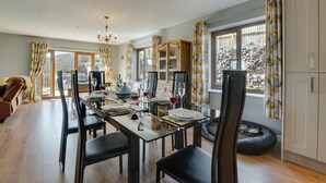A dining area with a long table set for four, flanked by black chairs, a black bean bag, and a wooden cabinet. - 3 Bed in Coelbren (oc-way238) (Coelbren)