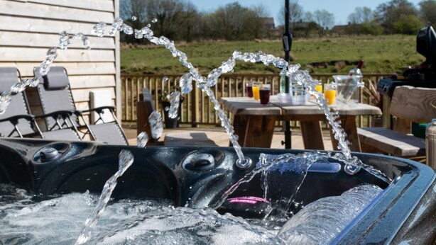 A hot tub with water flowing out, surrounded by outdoor furniture and a wooden deck. - 3 Bed in Coelbren (oc-way238) (Coelbren)