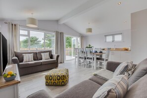 Ein modernes Wohnzimmer mit einer Couch, einem Hocker und einem Essbereich mit Stühlen und einem Tisch.
