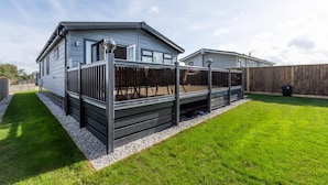 A mobile home with a fenced deck, a well-maintained lawn, and a clear sky. - 3 Bed in St. Merryn (oc-p00701) (Saint Merryn)