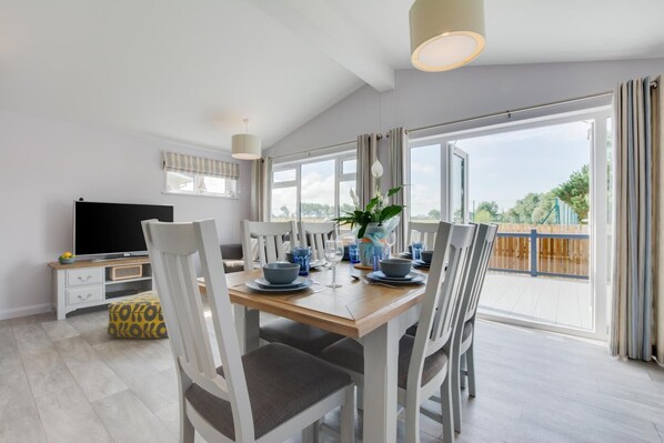 A dining area with a wooden table, white chairs, and a TV on a white cabinet.