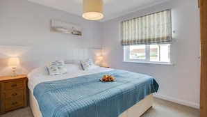 A bedroom with a bed, bedside tables, a window with curtains, a hanging light fixture, and a painting on the wall. - 3 Bed in St. Merryn (oc-p00701) (Saint Merryn)