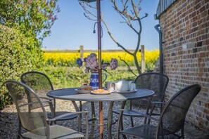 A round metal table with four chairs, a vase with flowers, a teapot, and a plate with food. - 2 Bed in Swanton Abbott (oc-1173) (Swanton Abbott)