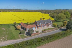 A two-story house with a garden and a field of yellow flowers in the background. - 2 Bed in Swanton Abbott (oc-1173) (Swanton Abbott)