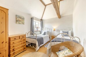 Un dormitorio con dos camas, un aparador de madera, una silla de mimbre y una ventana con cortinas.