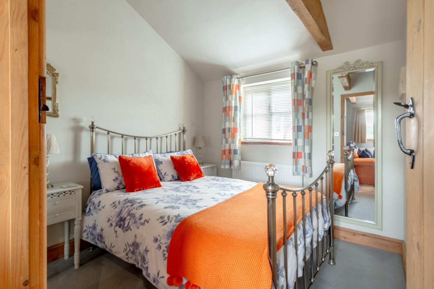 A bedroom with a bed, a nightstand, a mirror, and a window with curtains.