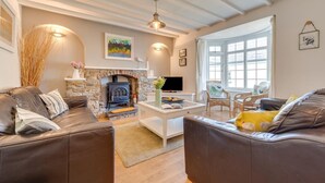 Ein gemütliches Wohnzimmer mit Kamin aus Stein, Ledersofas, einem Couchtisch und einem großen Fenster.