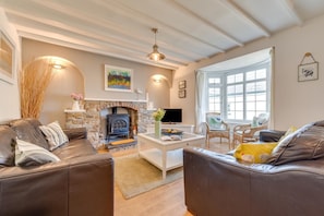 Ein gemütliches Wohnzimmer mit Kamin aus Stein, Ledersofas, einem Couchtisch und einem großen Fenster.