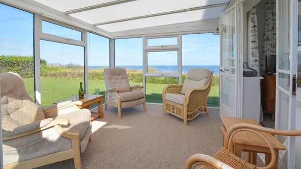A sunroom with large windows offering a view of the sea, furnished with wicker chairs and a sofa. - 3 Bed in Cromer (oc-1909) (Cromer)