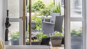 An open door leading to an outdoor patio with wicker furniture, potted plants, and a table. - 3 Bed in Cardiff (oc-bow65) (Cardiff)