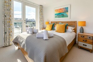 A hotel room with a bed, a nightstand, a window with curtains, and a painting on the wall.