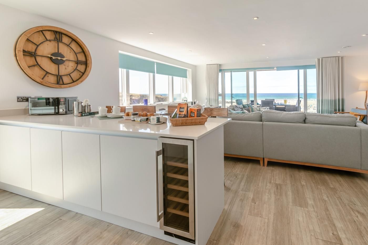 A modern kitchen with a large wooden clock, a built-in oven, and a view of the beach.