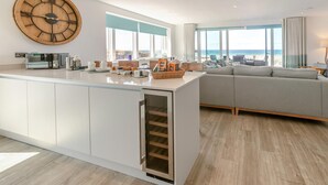A modern kitchen with a large wooden clock, a built-in oven, and a view of the beach. - 3 Bed in Perranporth (oc-p00695) (Perranporth)