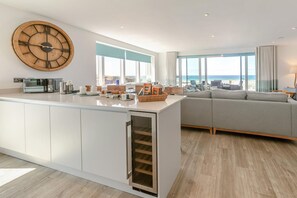 A modern kitchen with a large wooden clock, a built-in oven, and a view of the beach. - 3 Bed in Perranporth (oc-p00695) (Perranporth)