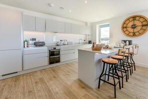 A modern kitchen with white cabinetry, a central island with stools, and a large wooden clock on the wall.