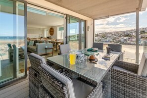 A sunlit terrace with a glass table, wicker chairs, and a view of the beach and town. - 3 Bed in Perranporth (oc-p00695) (Perranporth)