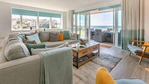 A modern living room with a sofa, coffee table, and a view of the ocean. - 3 Bed in Perranporth (oc-p00695) (Perranporth)
