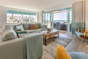 A modern living room with a sofa, coffee table, and a view of the ocean. - 3 Bed in Perranporth (oc-p00695) (Perranporth)