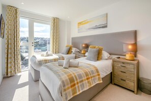 A hotel room with two beds, a large window, a city view, a painting, and a bedside table with lamps.