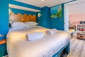 A hotel room with a large bed, two rolled towels, a wooden headboard, and a painting on the wall. - 5 Bed in Newquay (oc-p00894) (Newquay)