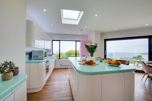 A modern kitchen with a central island, large windows, and a view of the sea. - 5 Bed in Newquay (oc-p00894) (Newquay)